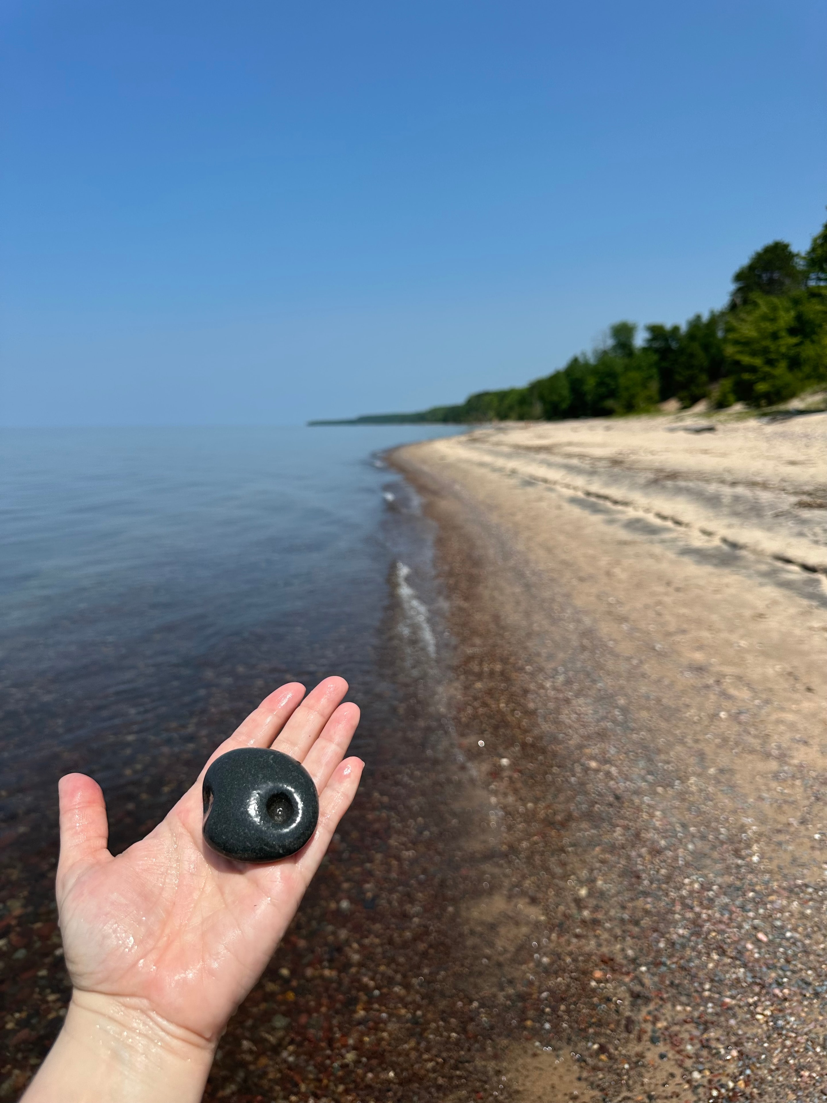 Dark stone with a natural hole held on a Lake Superior beach